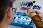 Kind mit Brille hält die Hand eines Erwachsenen, Blick auf blauen Kommunikationsbildschirm mit Symbolen für 'essen' und 'trinken'.