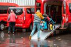 Person schiebt Rollstuhlfahrer eine Rampe hinab von einen roten Transporter mit der Aufschrift 'BeTraDi'.