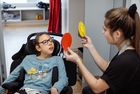 Frau hält zwei runde, eine rote und eine gelbe Karten, eine rot und eine gelb, vor ein Kind im Rollstuhl in einem Zimmer.