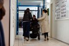 Drei Personen gehen einen Flur entlang, eine sitzt im Rollstuhl, die anderen beiden schieben den Rollstuhlfahrer.