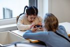 Ein Kind und eine Frau sitzen an einem Tisch, die Frau hält einen sprechenden Taster, das Kind schaut darauf.