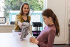 Unterrichtszimmer in der Blindenschule. Eine Frau reicht einem Mädchen einen Pullover.